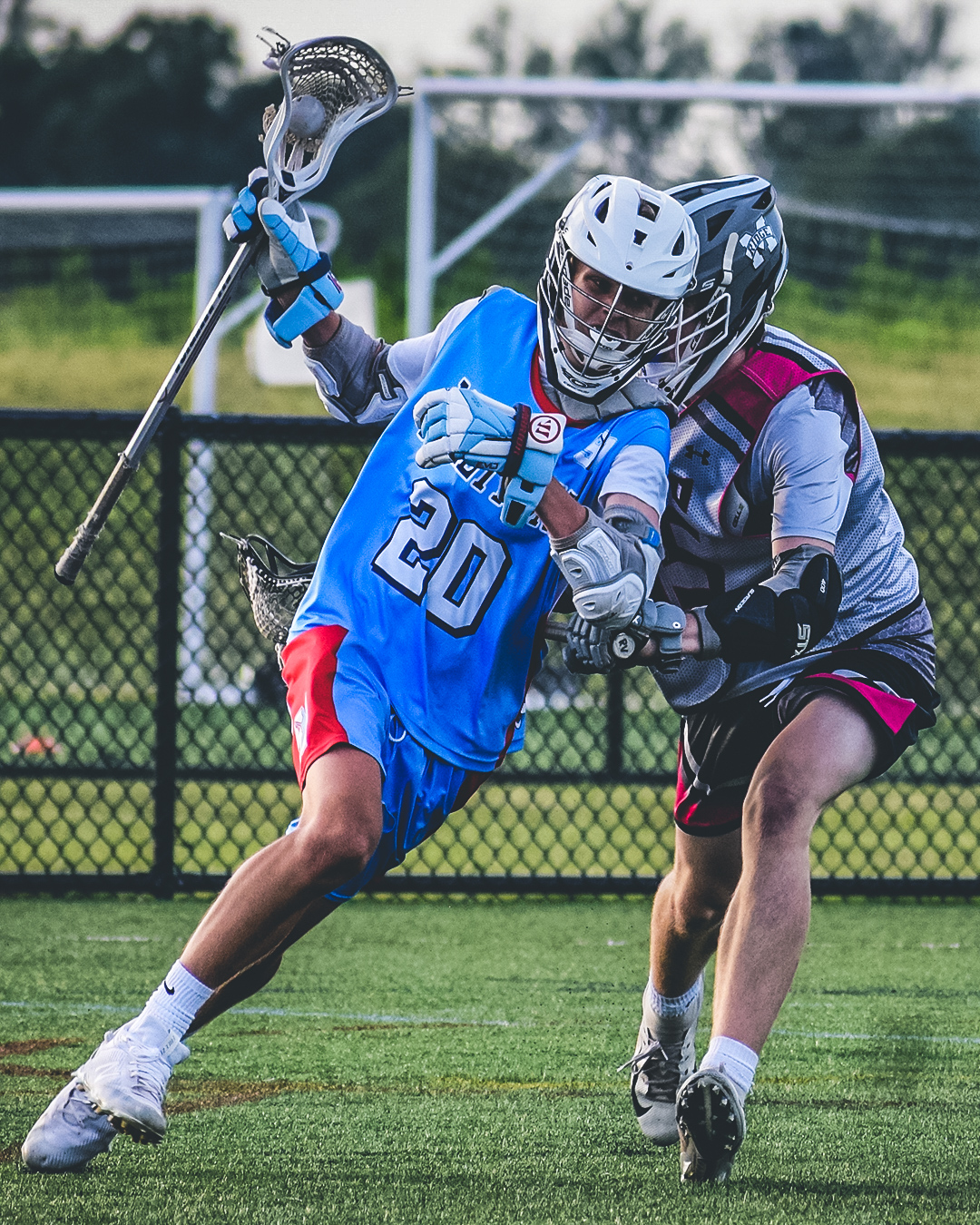A high-school-age Team 91 Carolina attackman in a Carolina-blue number 20 jersey driving to the goal past a defender.